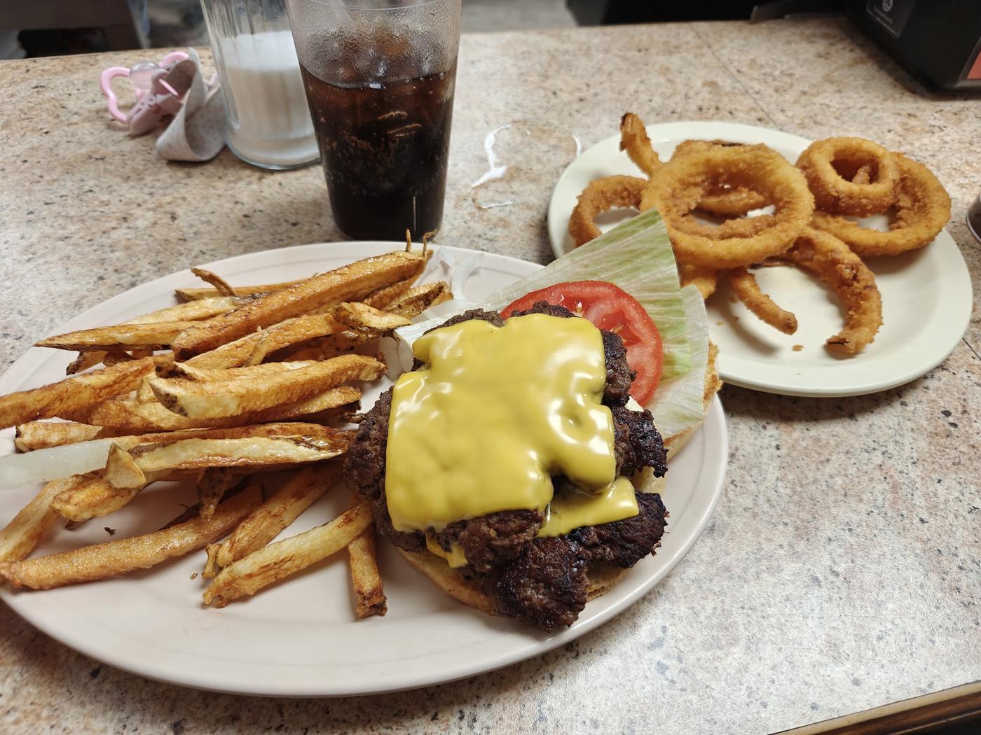 A cheeseburger with melted cheese beside a pile of hand-cut fries and a plate of onion rings on the counter at Bubba's